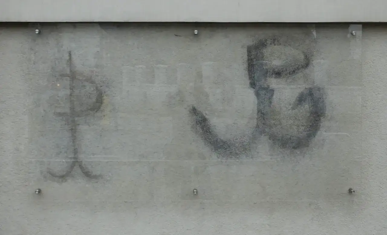 Znak Polski Walczącej, kotwica, namalowana na szarej ścianie. Symbol oporu i nadziei.