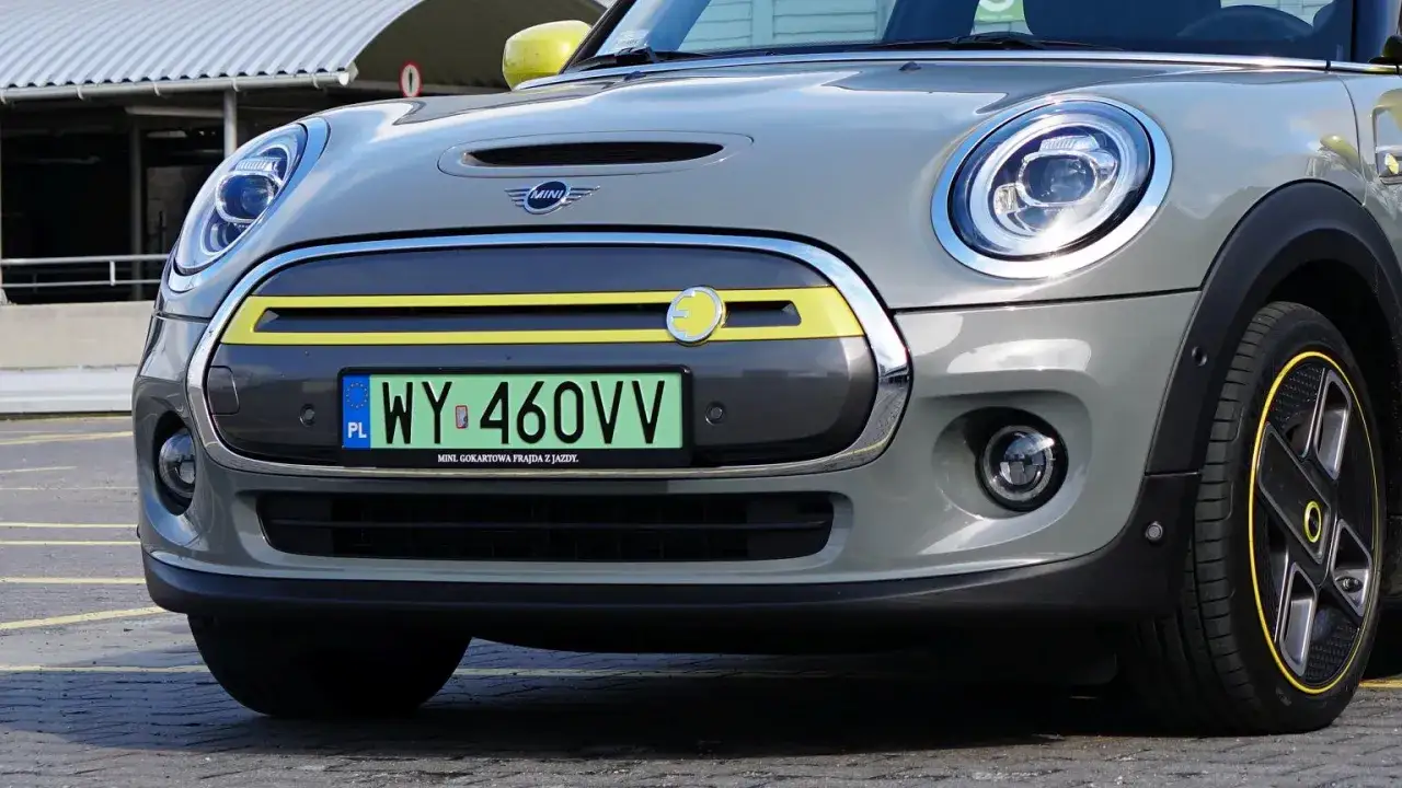 Szara elektryczna Mini Cooper z zieloną tablicą rejestracyjną.