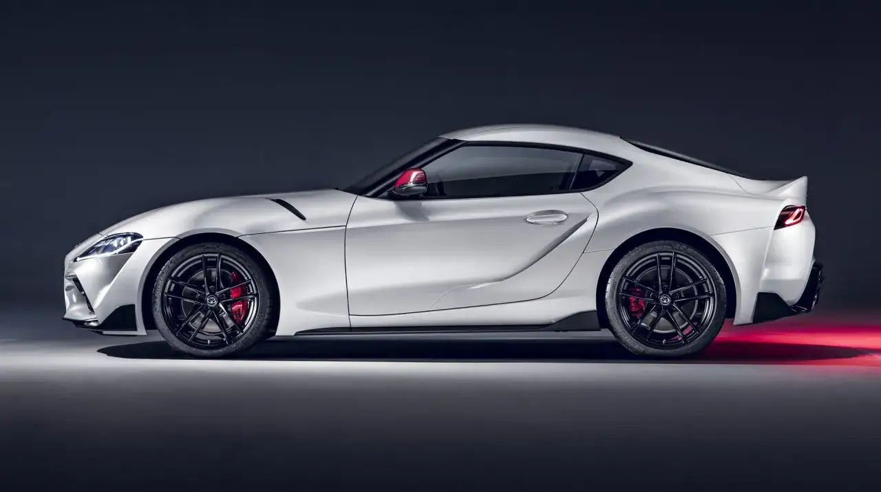 Biała Toyota GR Supra z czerwonymi zaciskami hamulcowymi i czarnymi felgami, prezentująca sportowy profil.