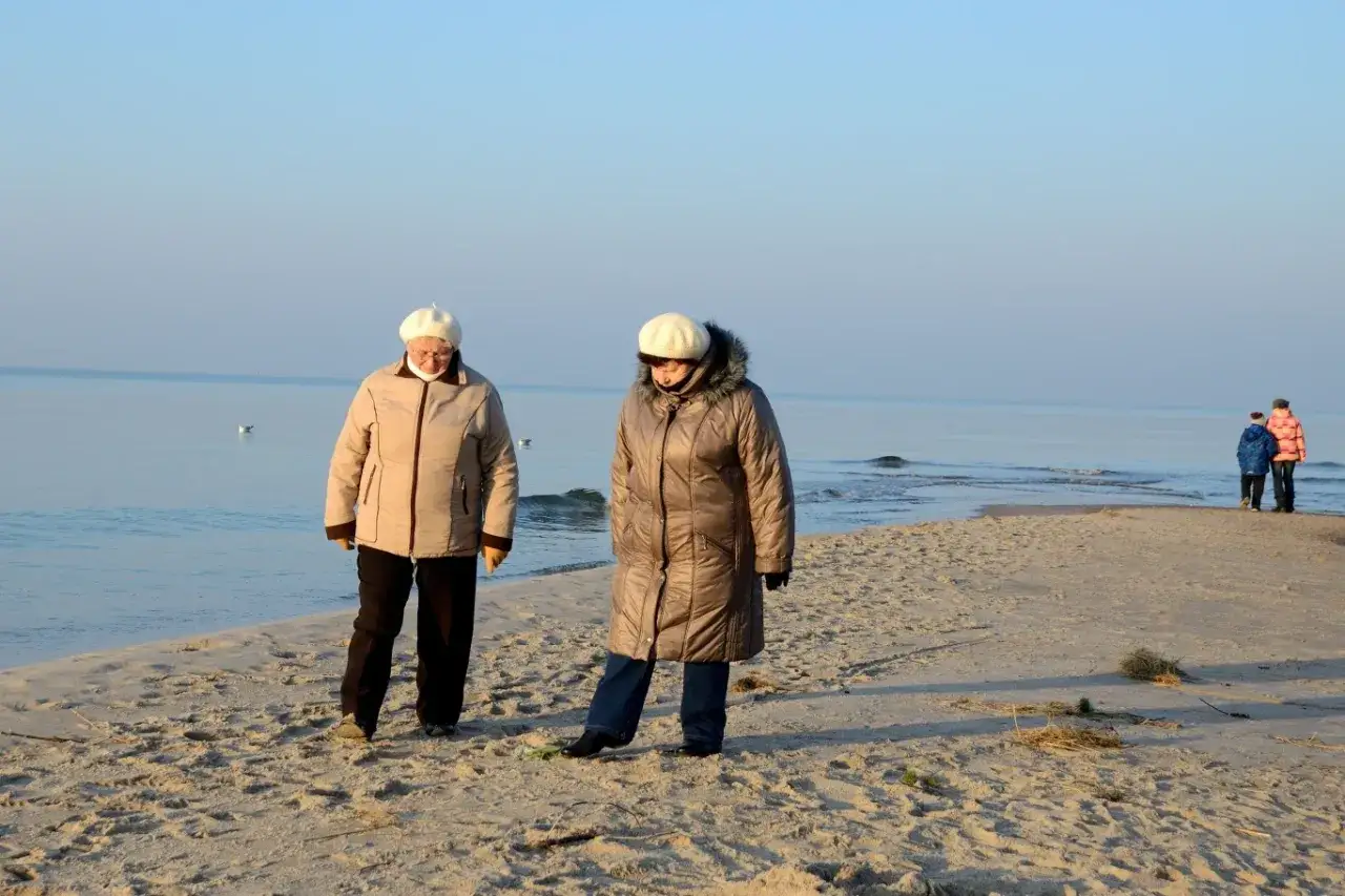 Dwie starsze panie spacerują po plaży, ciesząc się spokojem. Idealne tanie wycieczki dla seniorów nad morzem.