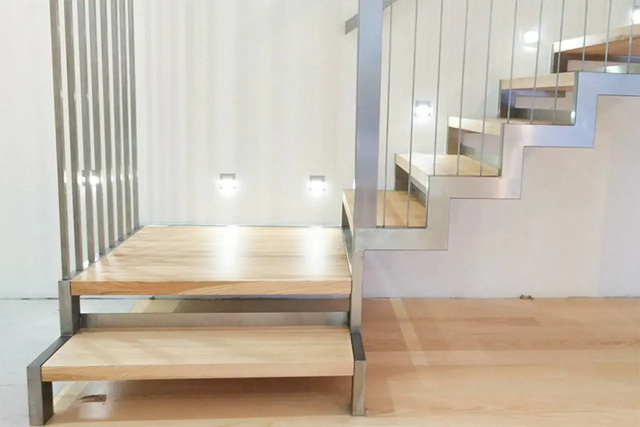 Nowoczesne schody z jasnego jesionu, z metalową balustradą i dyskretnym oświetleniem.