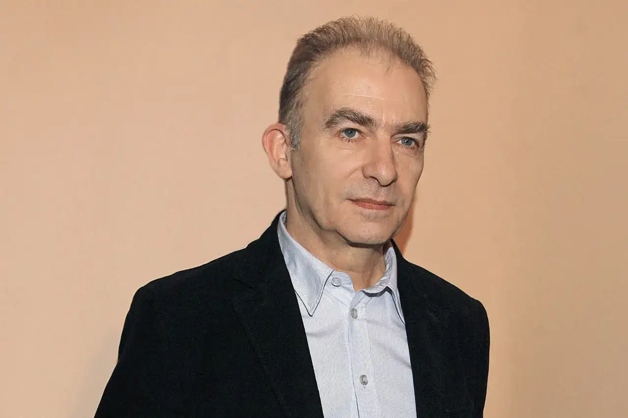 Portret mężczyzny w czarnej marynarce i jasnej koszuli. Sebastian Krajewski życie prywatne – jego spojrzenie sugeruje głębię przemyśleń.