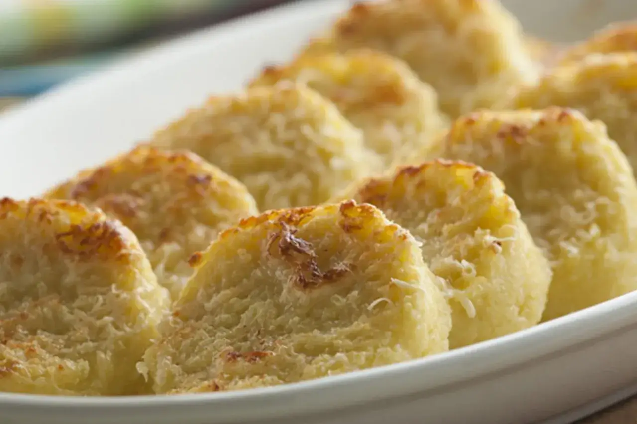 Gnocchi alla romana dorados y gratinados, servidos en una fuente blanca.