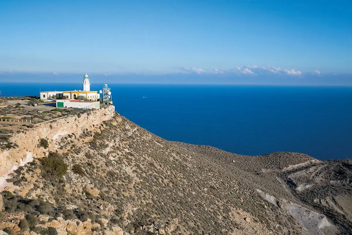 El mirador de Carboneras, con su faro y antenas, se alza sobre un acantilado rocoso con vistas al mar azul intenso.