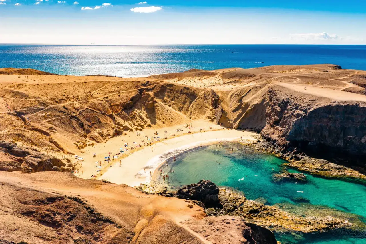 Traumhafte Bucht mit türkisfarbenem Wasser und goldgelbem Sand. Perfekt für die Packliste Lanzarote: Badesachen, Sonnencreme und gute Laune!