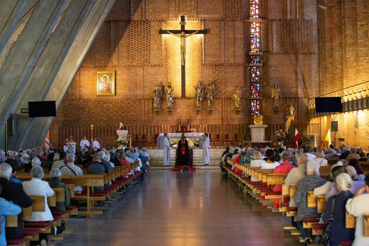 Wnętrze kościoła z wiernymi na ławkach. Na ścianie wisi krzyż, obrazy i rzeźby. Centralnie klęczy postać w czerni, symbolizująca głęboką dewocję.