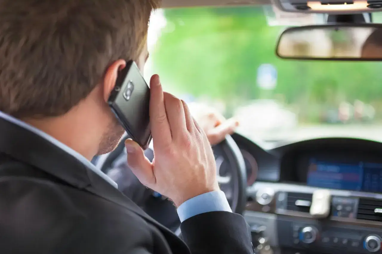 Mężczyzna w garniturze rozmawia przez telefon podczas jazdy. Ryzykuje mandat za telefon.