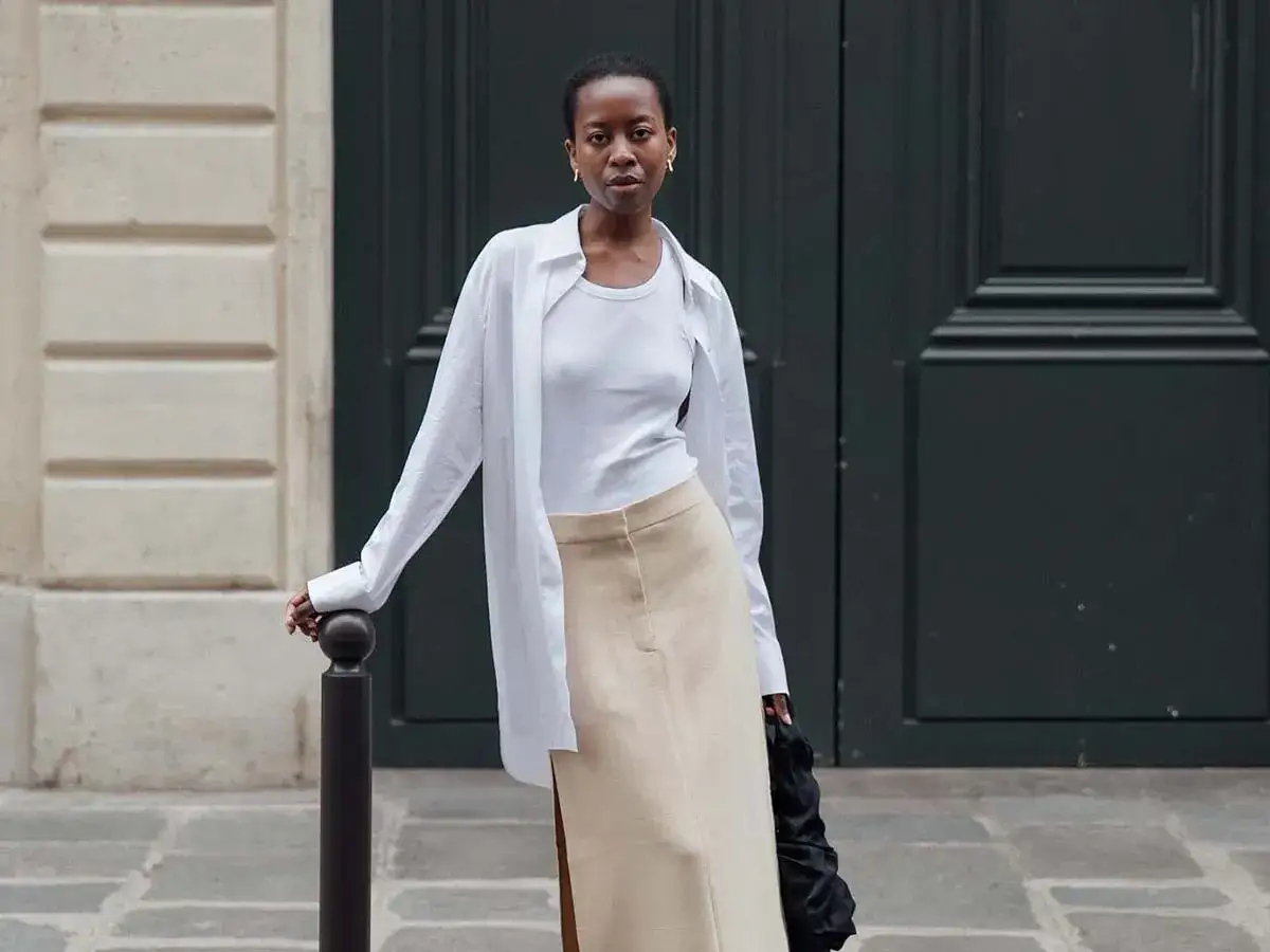 Mujer con un look minimalista, ideal para un armario c&aacute;psula. Falda beige y camisa blanca oversize.