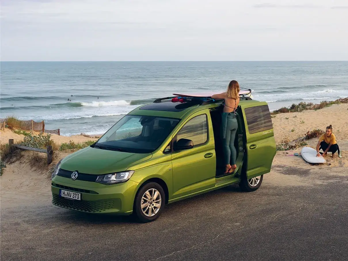 Un caddy tramper vert pr&ecirc;t pour l'aventure sur la plage, avec des surfeuses et leurs planches.