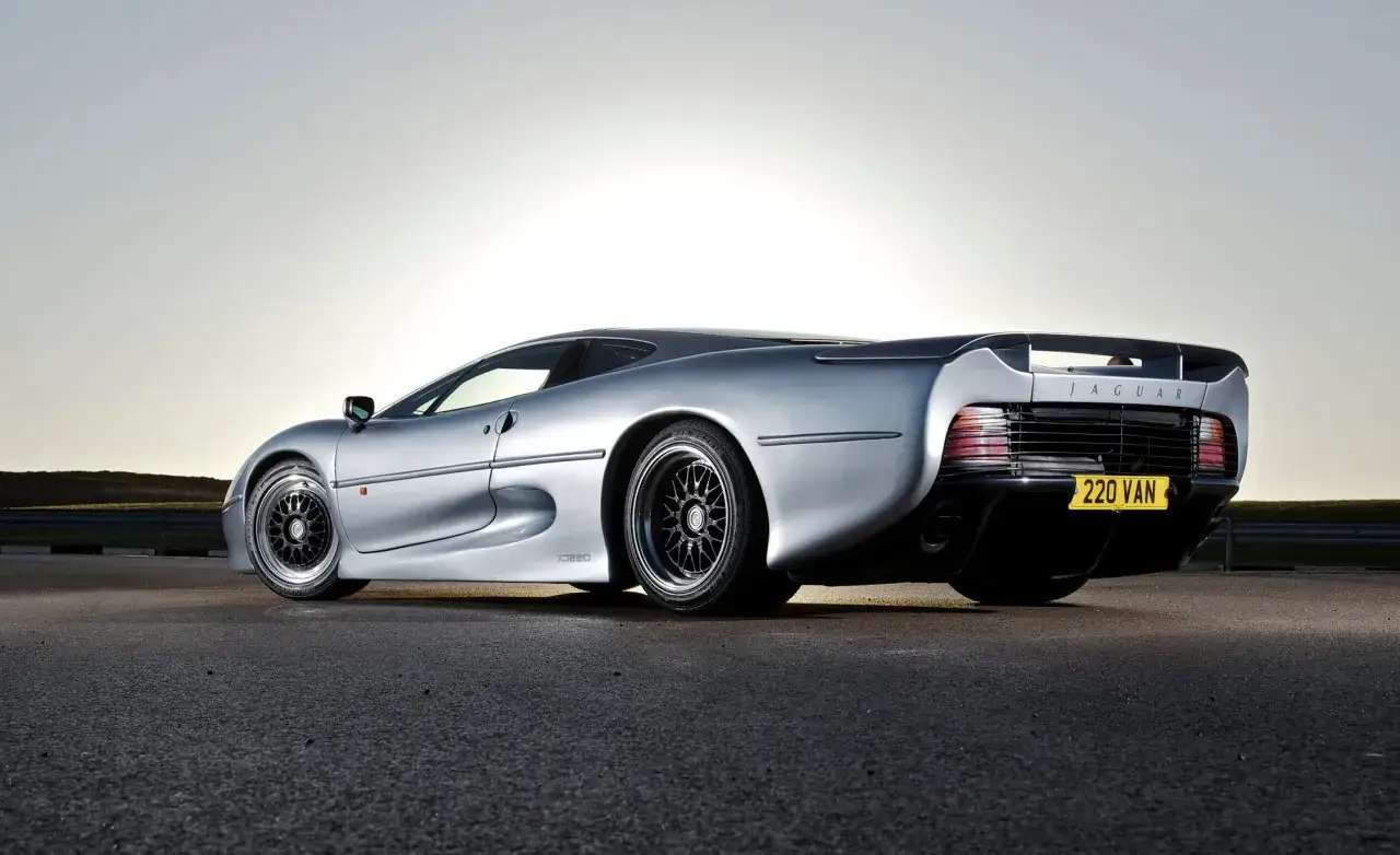 Srebrny Jaguar XJ220 z charakterystycznym spojlerem i felgami, gotowy do jazdy.