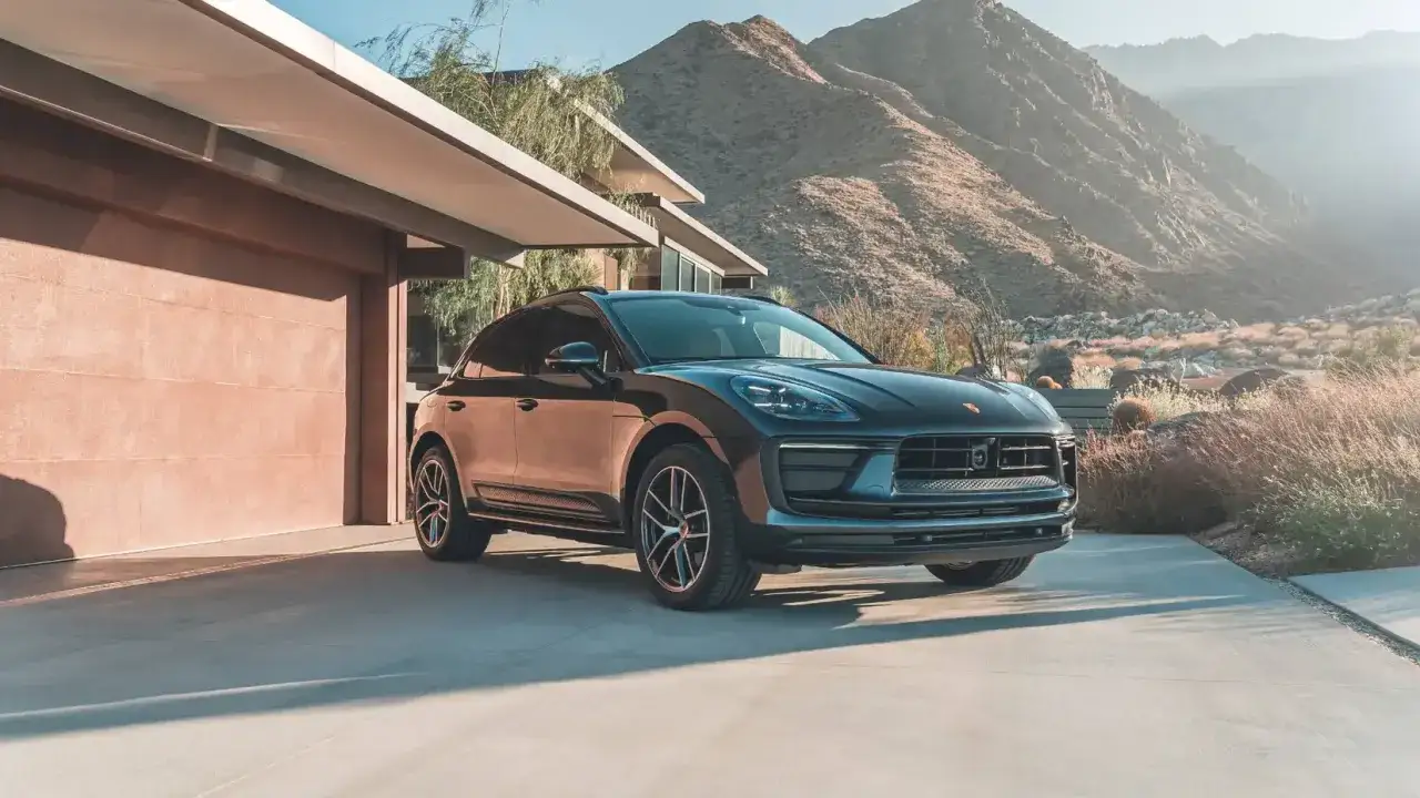 Ciemnoszary Porsche GTS zaparkowany przed nowoczesnym domem na pustyni, z górami w tle.