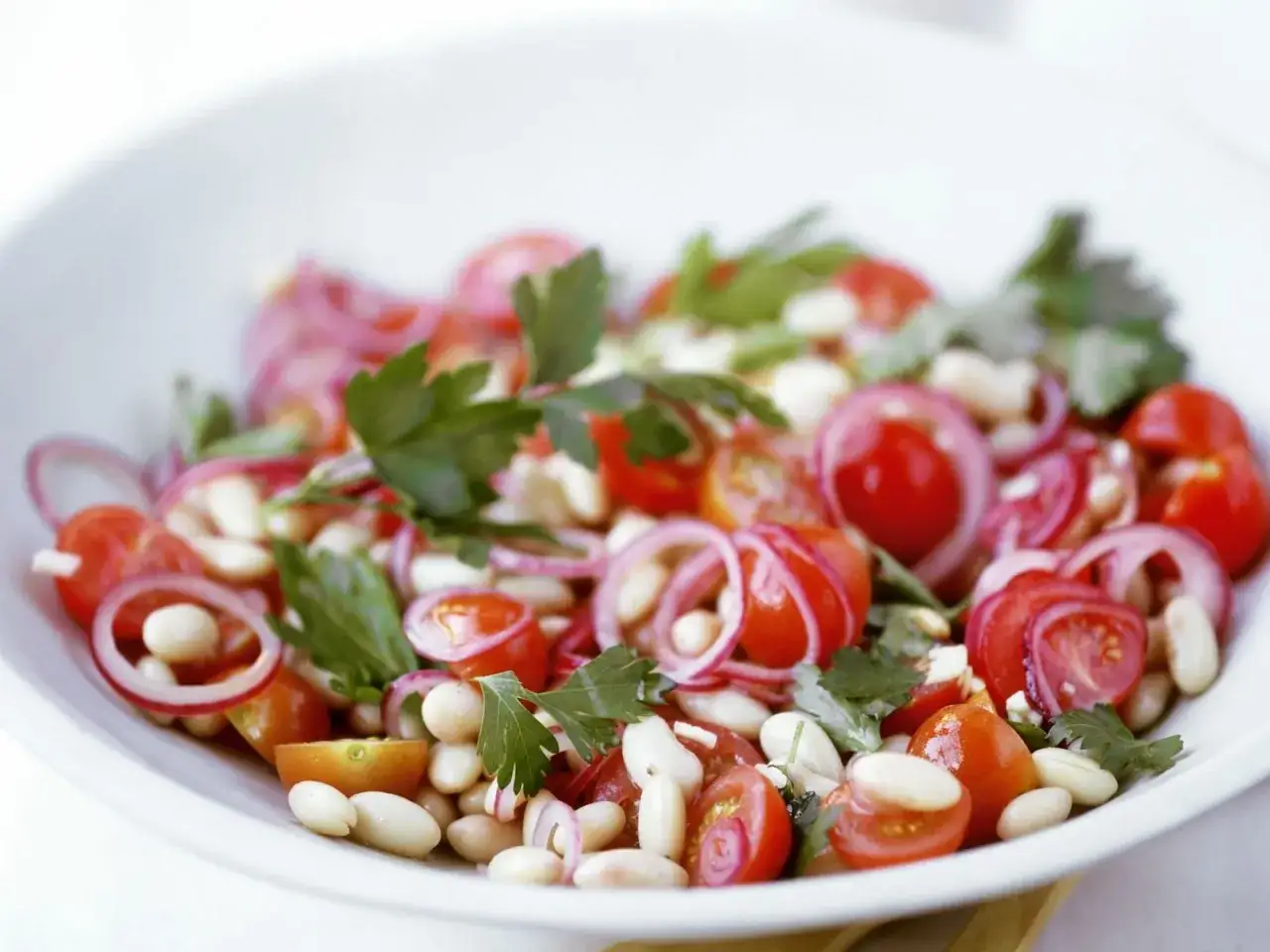 Ein frischer Bohnen Tomaten Salat mit roten Zwiebeln und Petersilie, appetitlich in einer weißen Schüssel angerichtet.