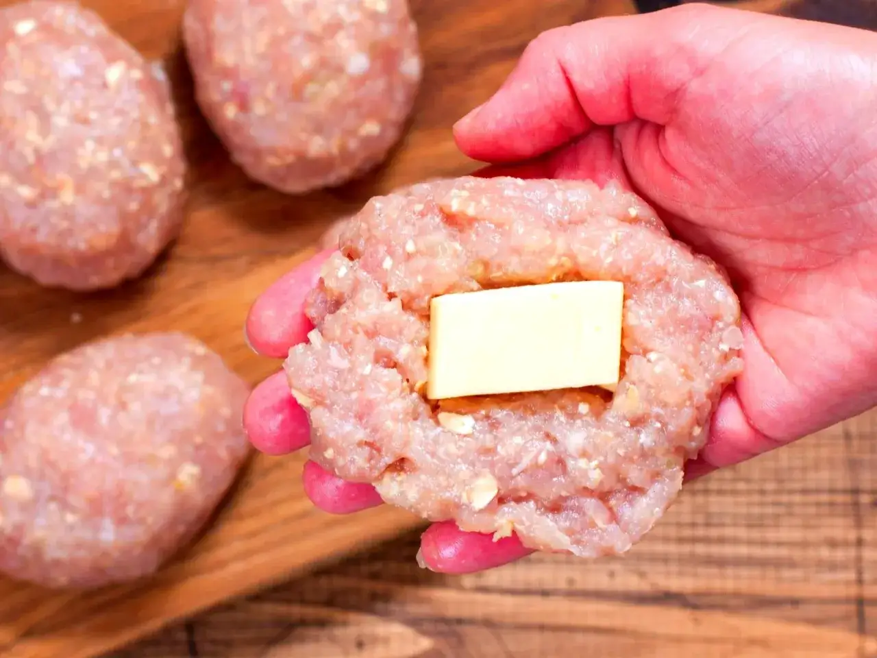 Ręka formuje mięso na burgery, dodając do środka kawałek masła.