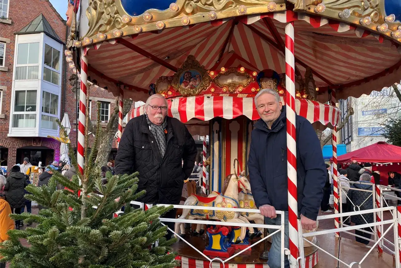 Zwei M&auml;nner stehen auf einem Karussell auf dem herten weihnachtsmarkt. Im Vordergrund steht ein Weihnachtsbaum.