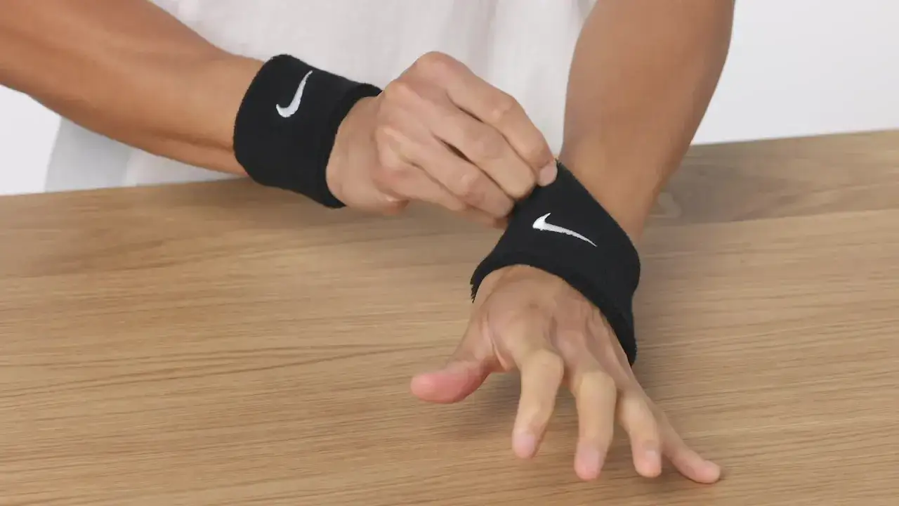 Dłoń zakłada czarną opaskę na rękę Nike z białym logo. Gotowy do treningu!