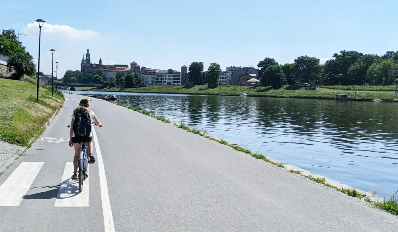 Dziewczyna na rowerze przemierza wiślaną trasę rowerową w Krakowie, podziwiając Wawel.