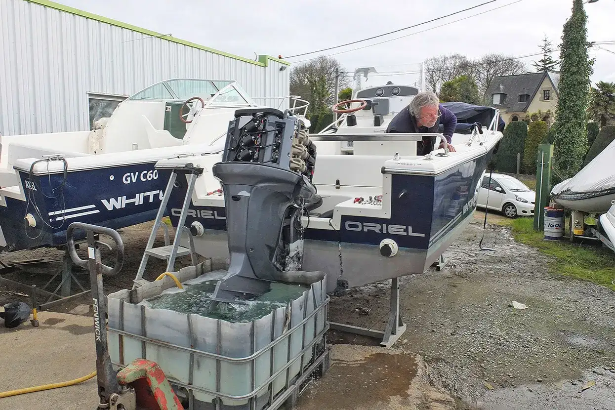 Un homme effectue le rinçage moteur hors bord vinaigre blanc d'un bateau. L'hélice est immergée dans une cuve remplie de liquide.