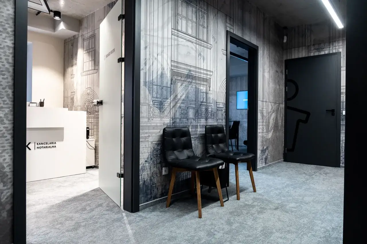 Nowoczesna Kancelaria Notarialna. W poczekalni dwa czarne fotele, ściany z grafiką architektoniczną. Dowiedz się, jak zwracać się do notariusza.
