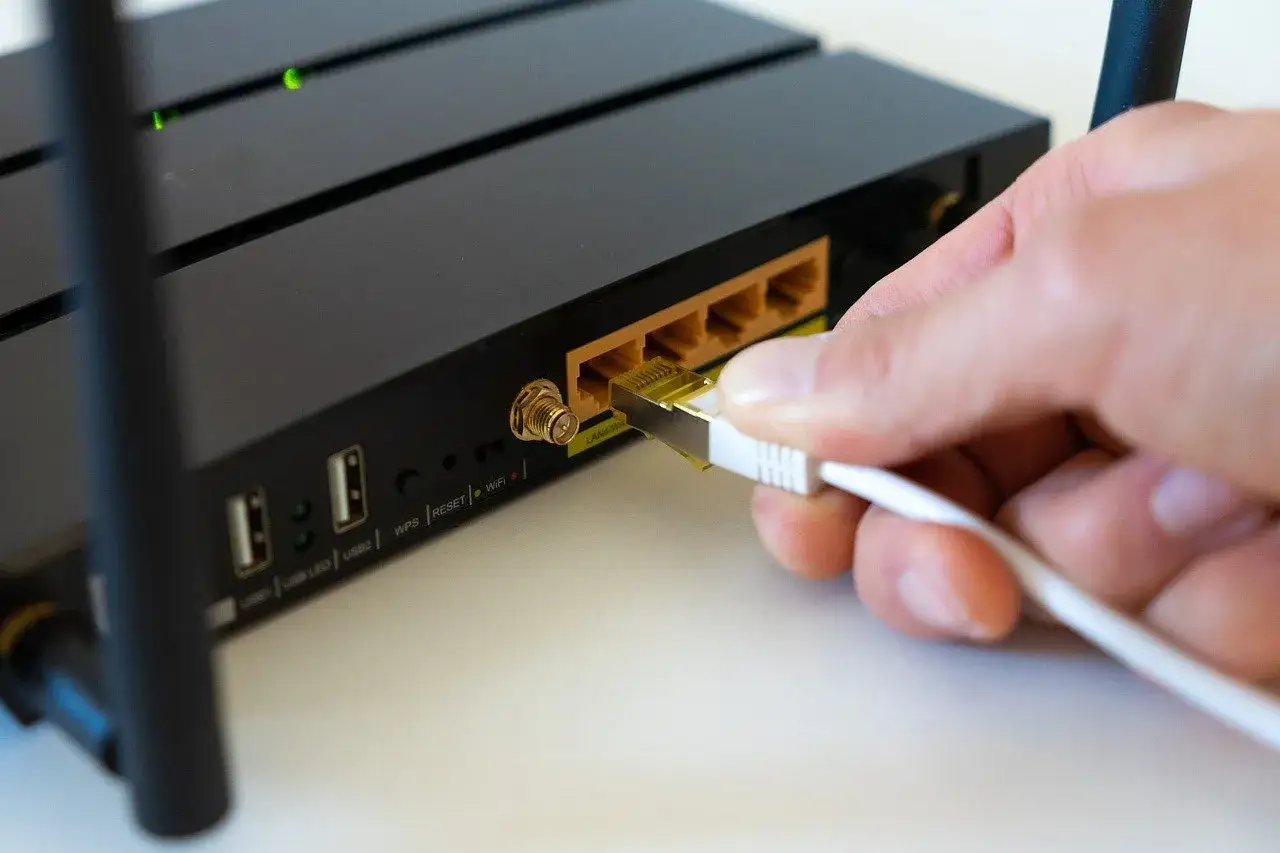 Dłoń wkłada kabel do routera. Widoczny przycisk RESET, który pomoże Ci dowiedzieć się, jak zresetować router.