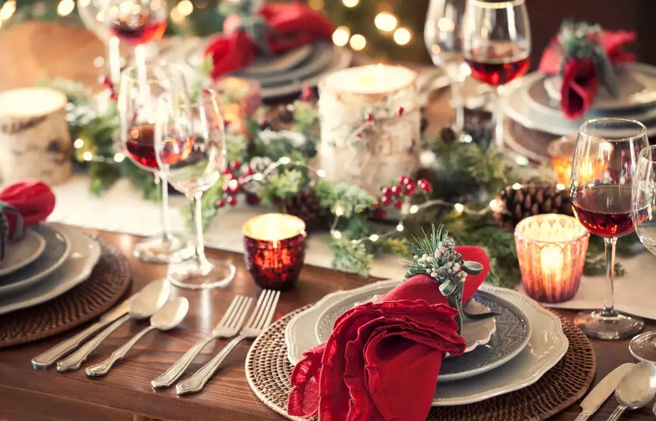 Elegant Christmas tablescapes with red napkins, pinecones, berries, and glowing candles set a festive mood.