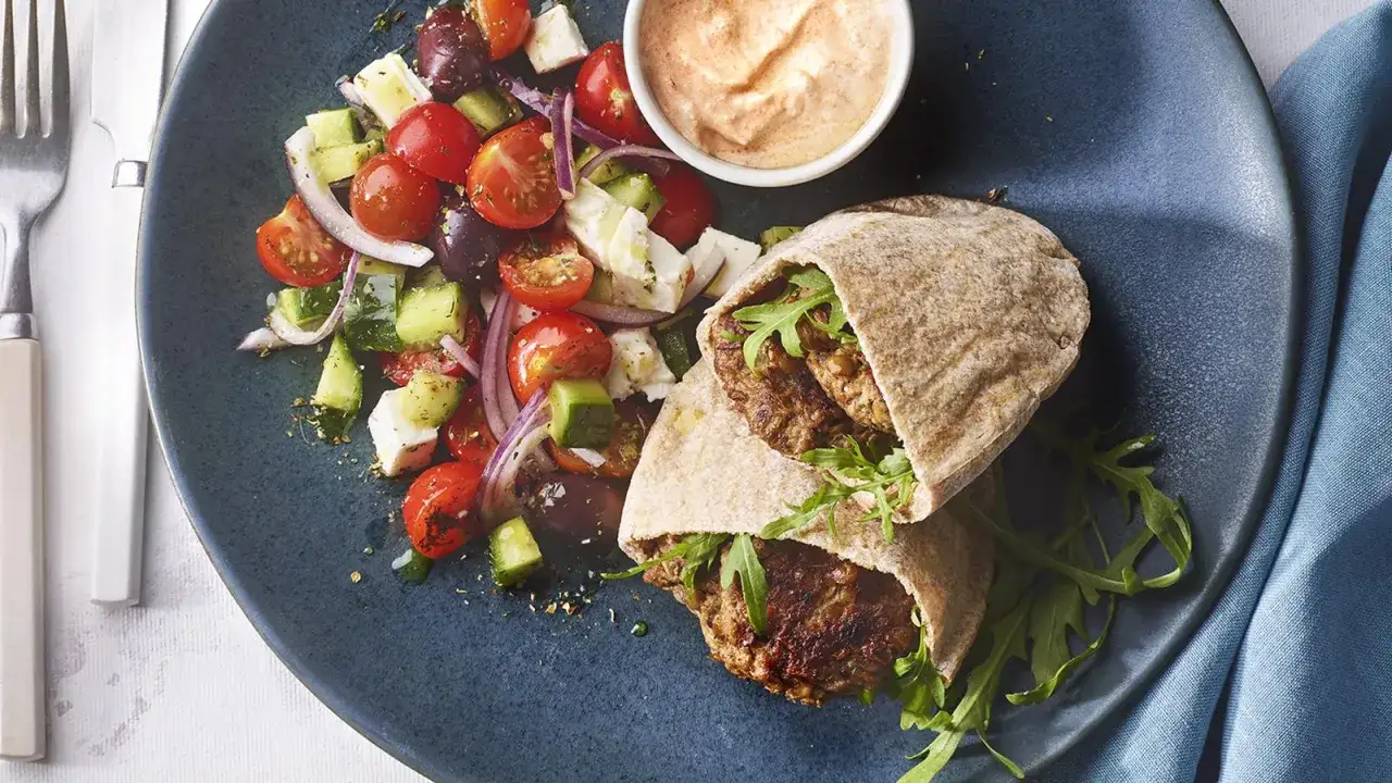 Deliciosa hamburguesa de lentejas en pan de pita, acompañada de ensalada griega y salsa.