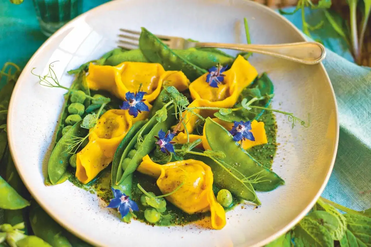 Ravioli gialli con piselli, fave e un tocco di borragine verdura, guarniti con fiori blu.