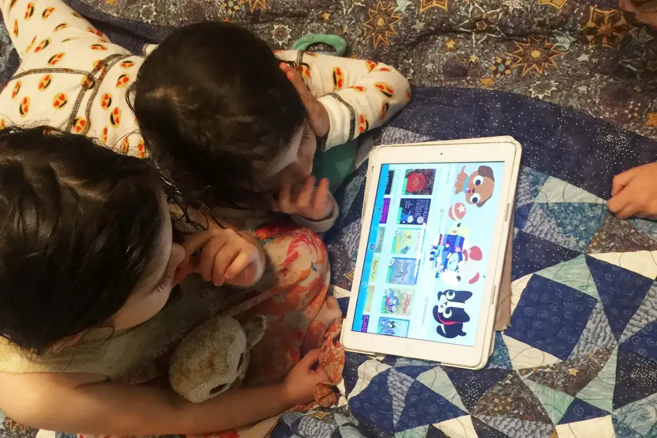 Dos niños exploran aplicaciones educativas para niños en una tablet, rodeados de mantas.