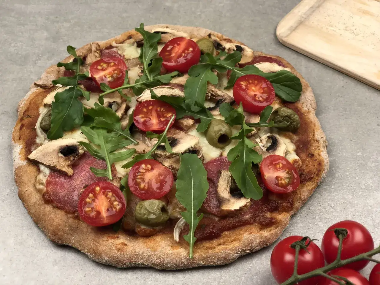Apetyczna pizza dla cukrzyka z pełnoziarnistym spodem, pomidorkami, rukolą i pieczarkami.