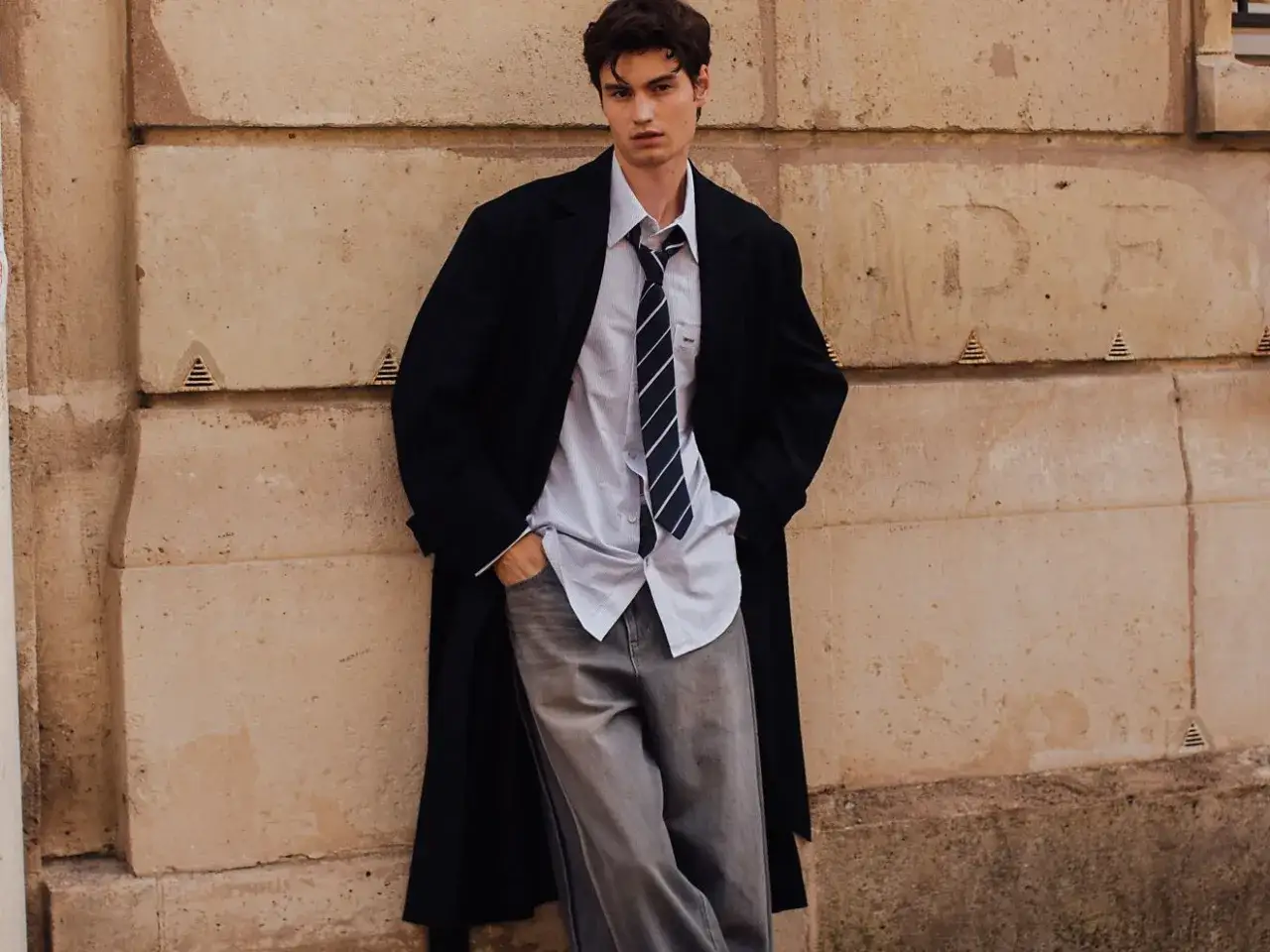 Ragazzo con un outfit moderno: camicia a righe, cravatta, cappotto lungo e baggy jeans uomo.