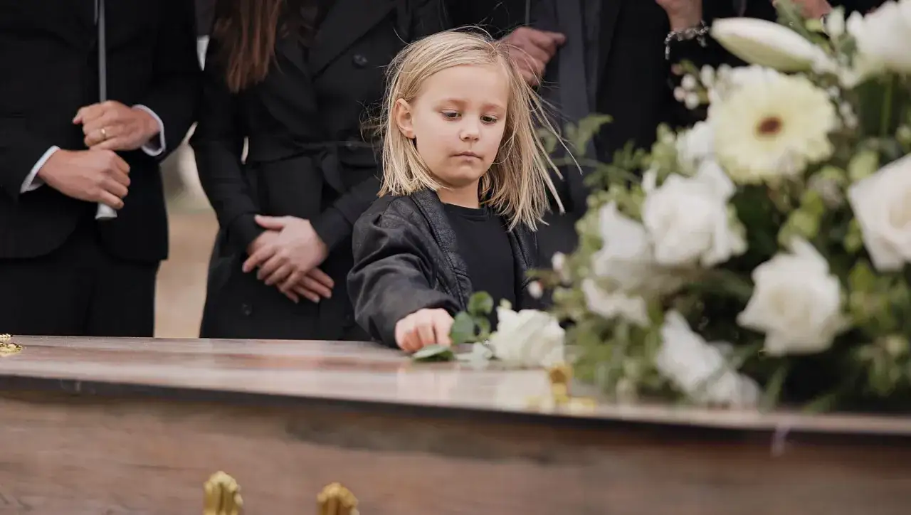Smutna dziewczynka kładzie różę na trumnie. Trudne pytanie: od jakiego wieku dziecko na pogrzebie jest właściwe?