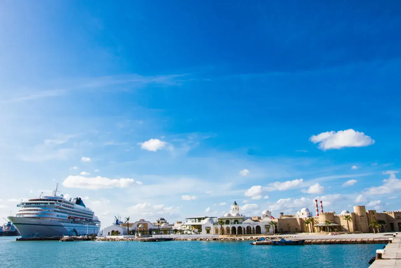 La Goulette, Tunisia: cosa vedere? Un porto con una nave da crociera e un complesso di edifici bianchi con cupole e mura di pietra.