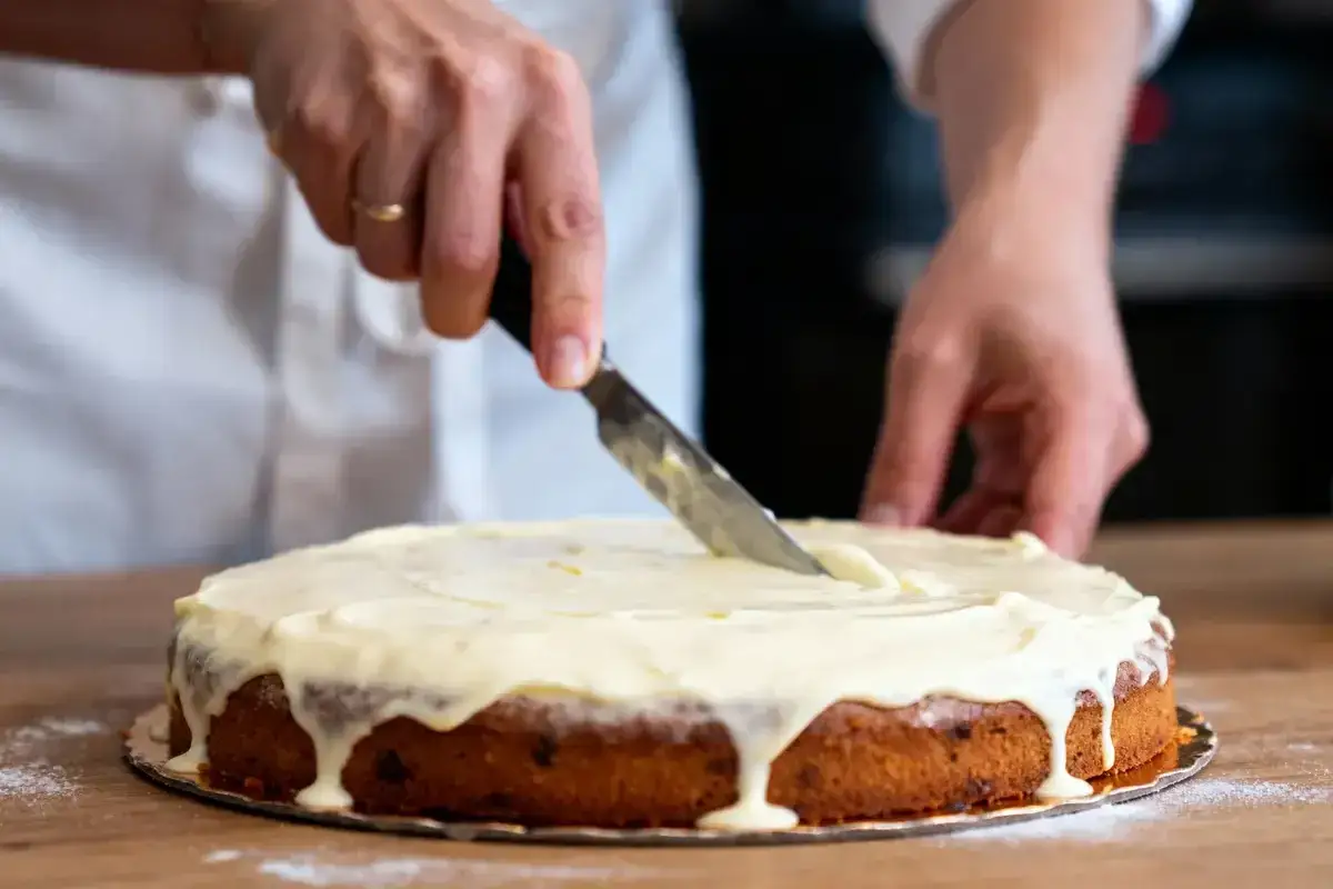Un chef étire le glaçage sur un gâteau, prêt à être dégusté, qu'il soit glacage sur gateau froid ou chaud.