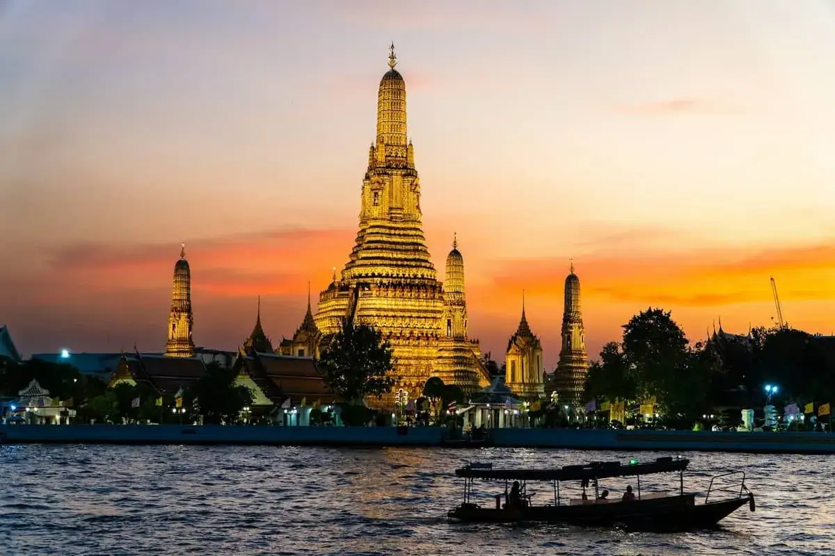 Il **tempio dell'alba Bangkok** splende dorato al tramonto, con un battello che naviga sul fiume Chao Phraya.