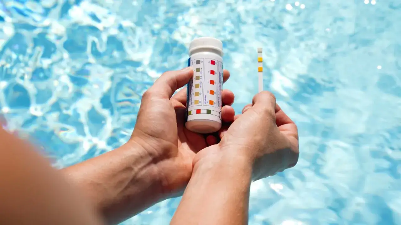 H&auml;nder h&aring;ller ett testkit f&ouml;r att m&auml;ta vattenkvaliteten i en pool. Teststickan visar f&auml;rger som indikerar om vattnet &auml;r grumligt.