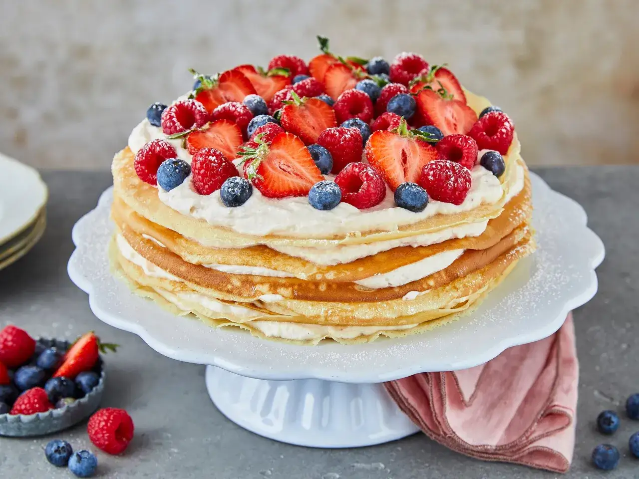 Eine &uuml;ppige Pfannkuchen Torte, geschichtet mit Sahne und garniert mit frischen Erdbeeren, Himbeeren und Blaubeeren.