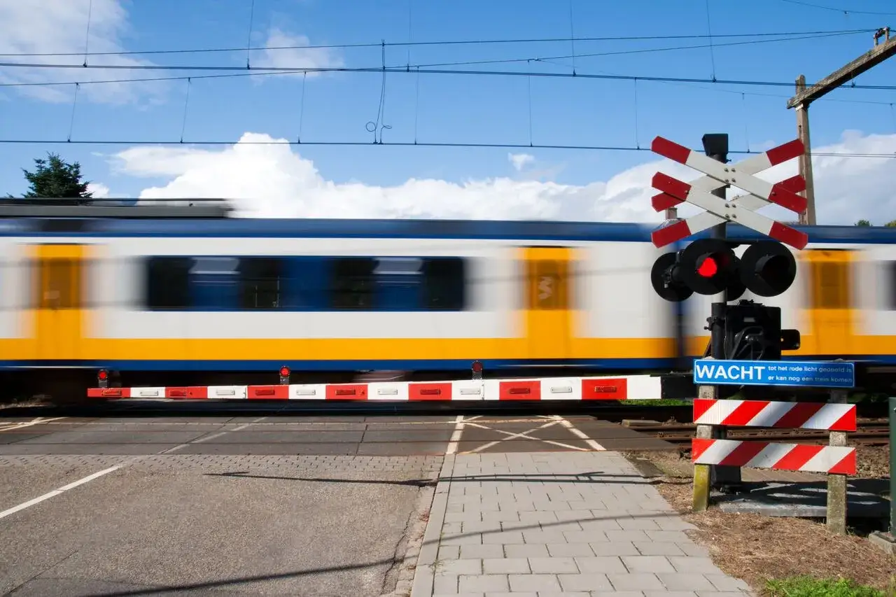 Pędzący pociąg mija przejazd kolejowy z zaporami. Czerwone światło sygnalizuje nadjeżdżający pociąg.