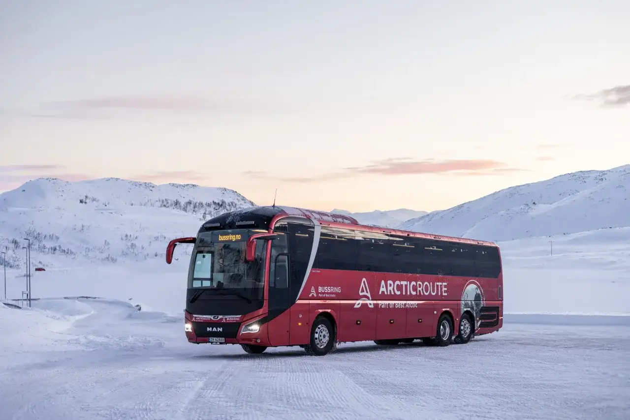 R&ouml;d buss fr&aring;n Arctic Route st&aring;r parkerad i sn&ouml;landskap. Kanske &auml;r det h&auml;r resan b&ouml;rjar f&ouml;r en t&aring;g till Lofoten-upplevelse.