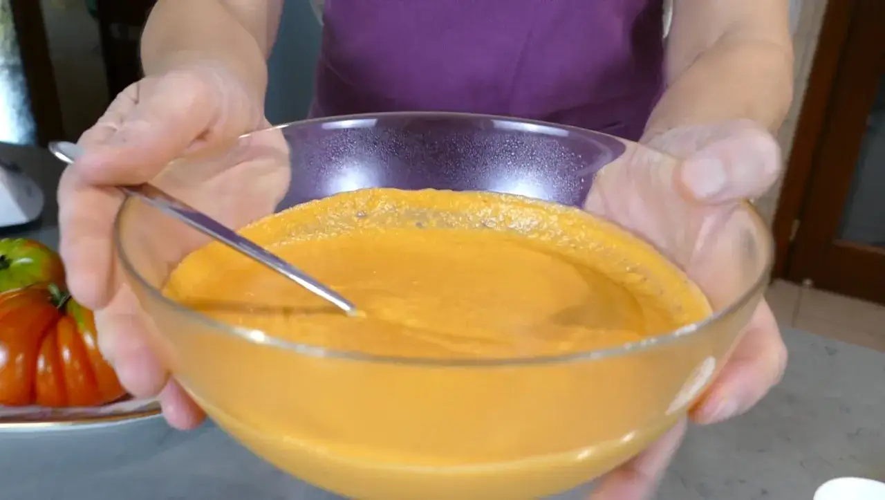 Mani che sorreggono una ciotola di vetro con una cremosa maionese di pomodoro, pronta per essere gustata.