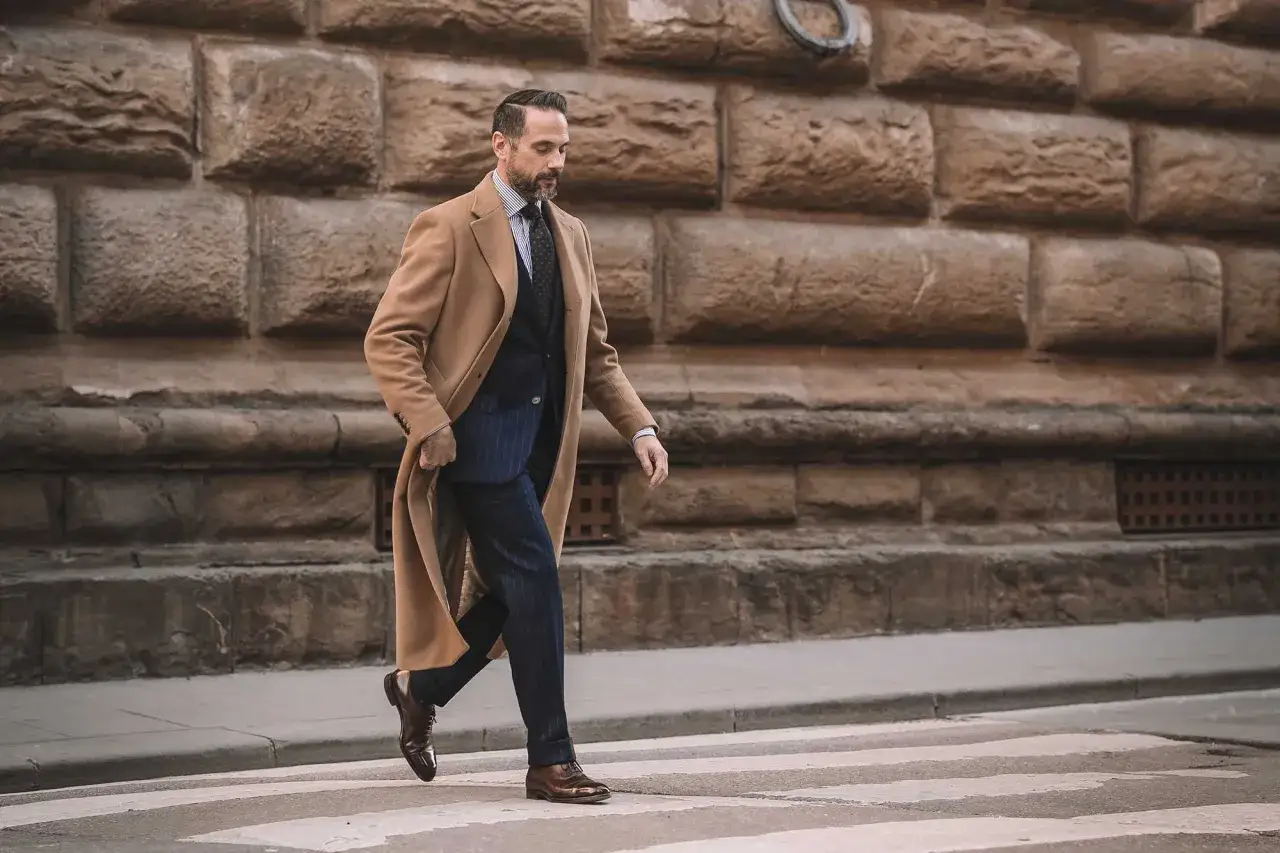 A man strides across a crosswalk in a stylish camel coat, a perfect example of sophisticated coats to wear with a suit.