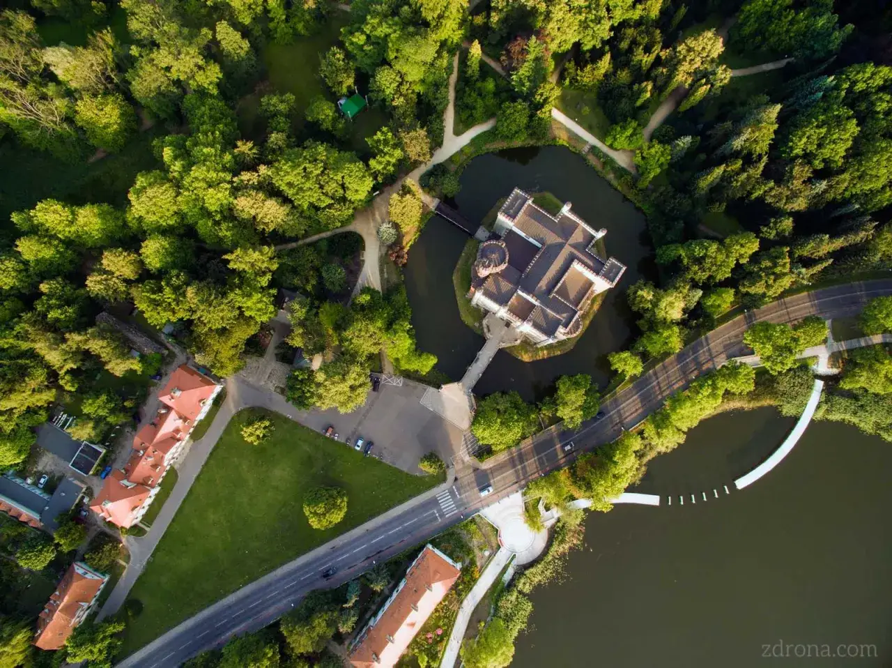 Zamek w Kórniku otoczony fosą i bujną zielenią, widziany z lotu ptaka. Malowniczy widok na architekturę i otaczający park.