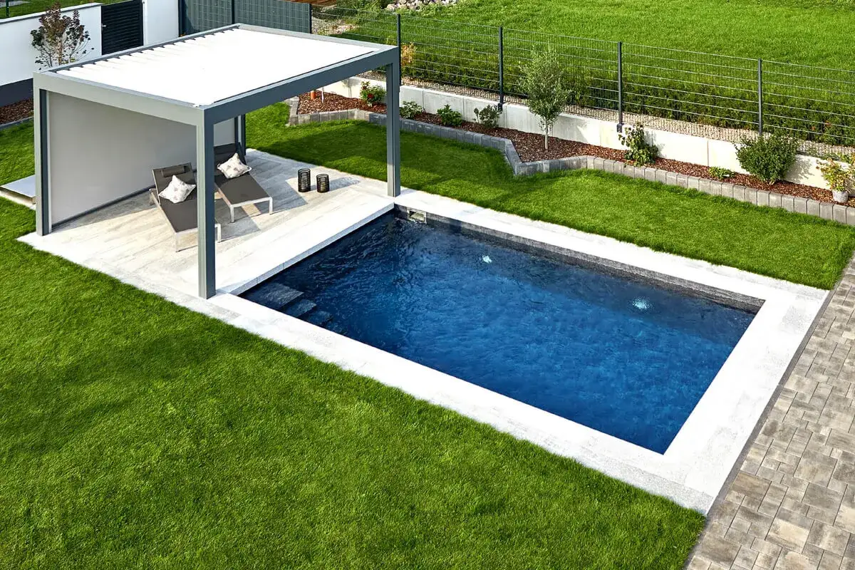 Elegante piscina de obra rectangular con cubierta moderna, tumbonas y césped verde. Un ejemplo de diversos tipos de piscinas de obra.