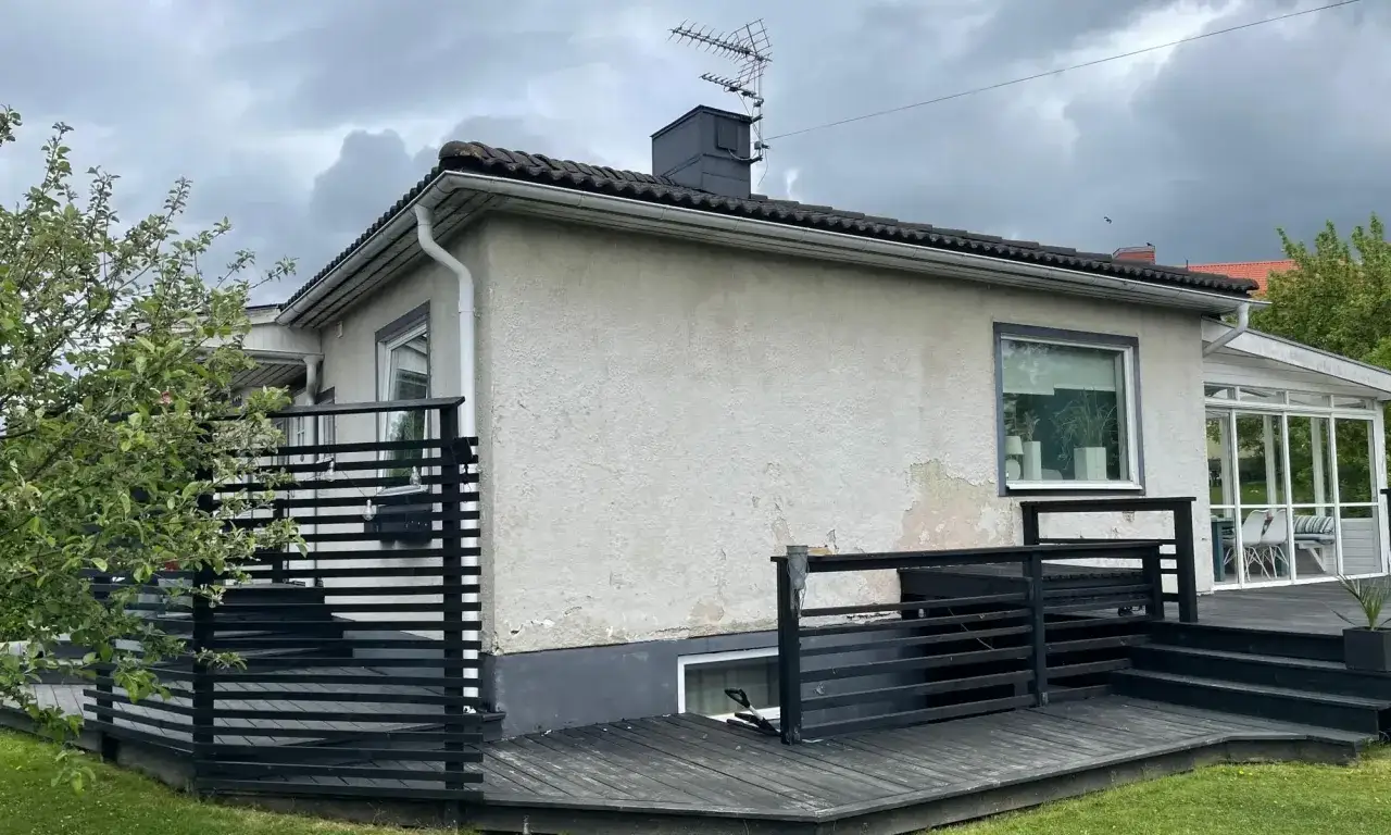 Ett hus med grå putsad fasad och en svart träaltan. En antenn syns på taket.