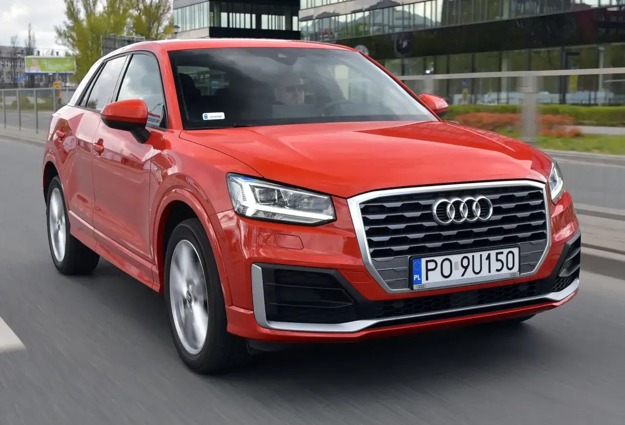 Czerwone Audi Q2 w ruchu miejskim. Choć jego kompaktowe wymiary to zaleta, niektórym mogą przeszkadzać wady, jak ograniczona przestrzeń z tyłu.