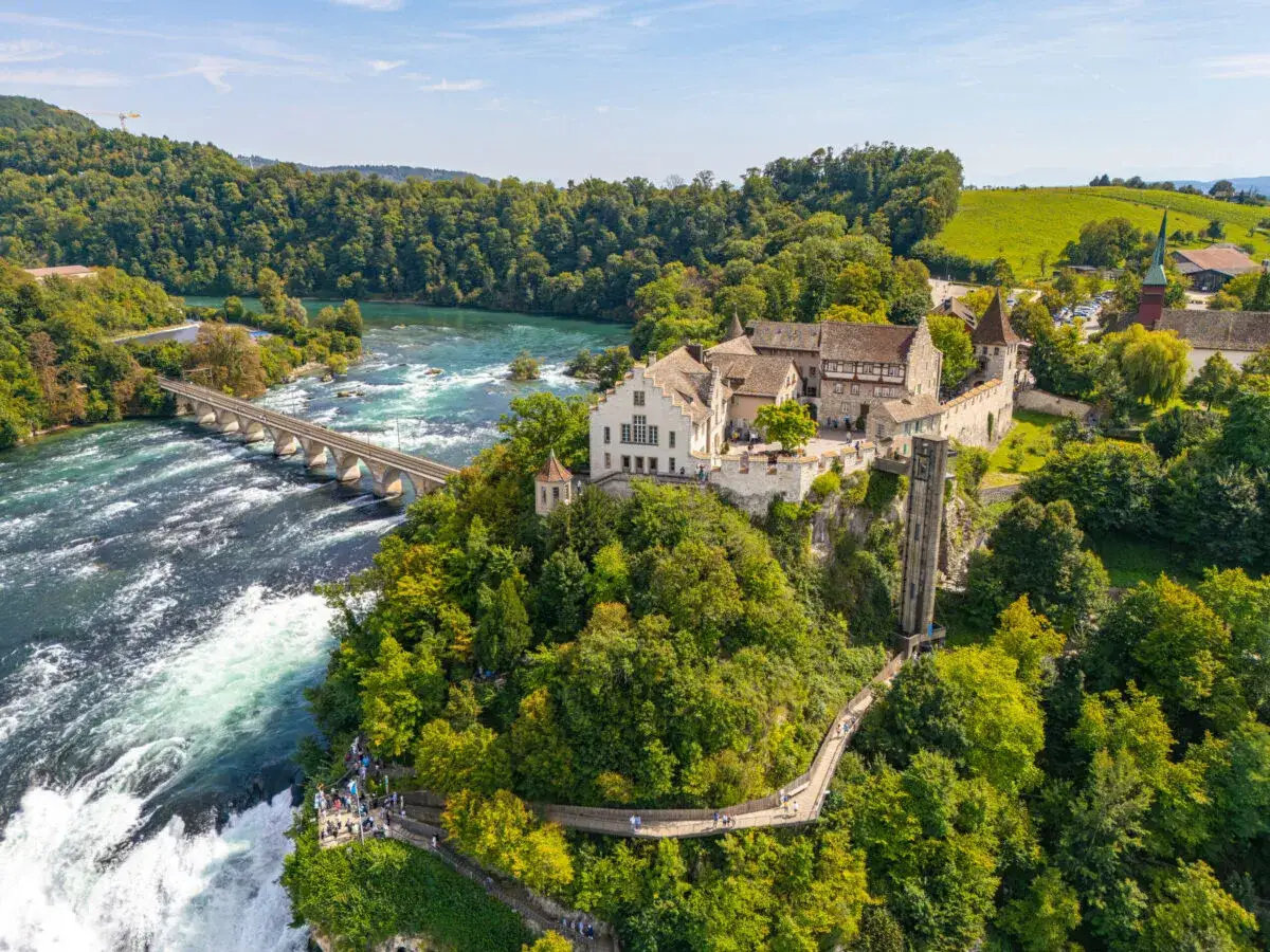 Majestätische Rhein Wasserfälle mit Schloss Laufen, das über dem tosenden Wasser thront. Eine Brücke überspannt den Fluss.