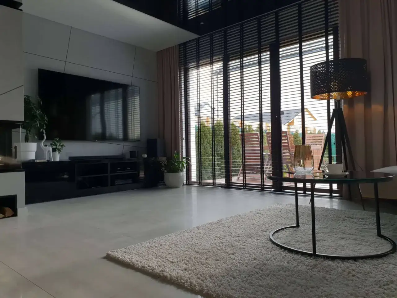 Nowoczesny salon z dużym oknem zasłoniętym drewnianymi żaluzjami czy roletami, które tworzą przytulną atmosferę.