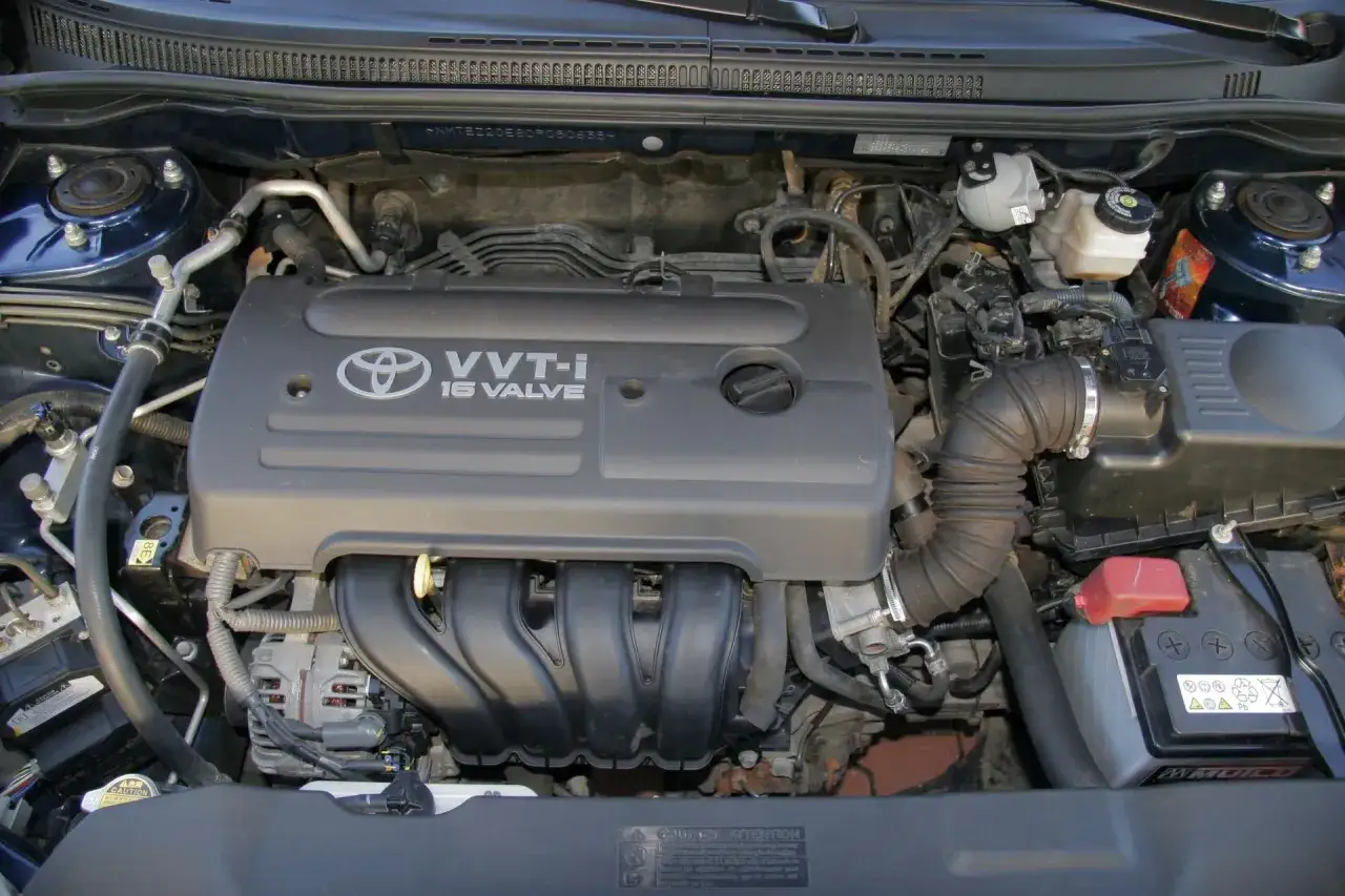 Silnik VVT-i 16 Valve z Toyoty Corolla E12. Widoczny alternator, akumulator i elementy układu dolotowego.