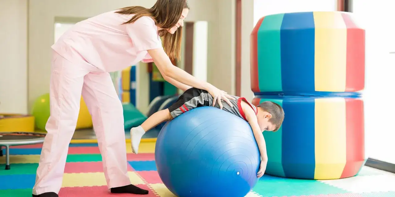 Fizjoterapeuta pomaga dziecku z zaburzeniami czucia głębokiego u dzieci objawy, ćwicząc na dużej, niebieskiej piłce.