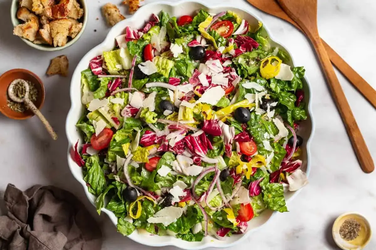 Frischer, bunter italienischer Salat mit knackigem Salat, Tomaten, Oliven, roten Zwiebeln und Parmesan. Perfekt für ein leichtes Mittagessen.