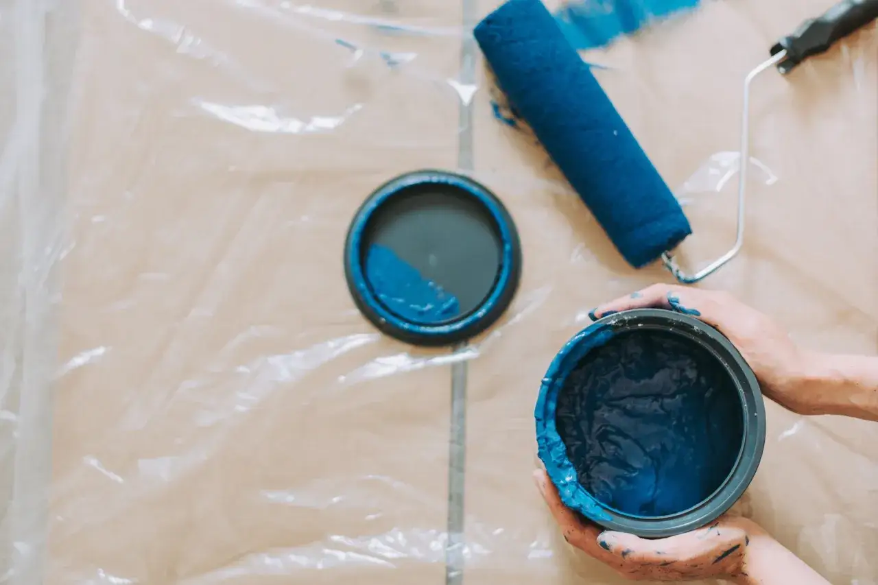 Mani sporche di vernice blu, un rullo e due barattoli pronti per dipingere.