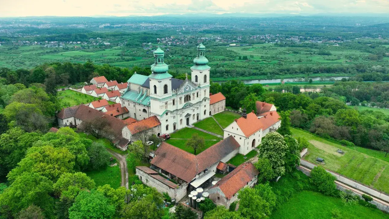 Klasztor Ojców Kamedułów na Bielanach, majestatyczna budowla z zielonymi kopułami, otoczona bujną zielenią i rozległym krajobrazem.